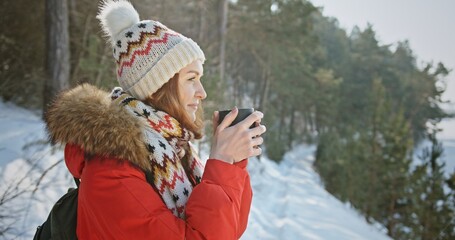 Woman backpacker traveler camper drinking hot tea and relaxing in winter forest, beautiful snow landscape on sunny day. Health care, authenticity, sense of balance. 4 K video