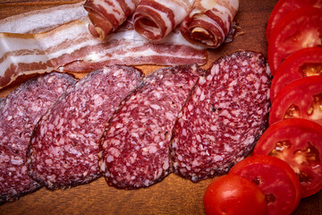 raw smoked sausage and bacon slices with tomato slices on a wooden tray