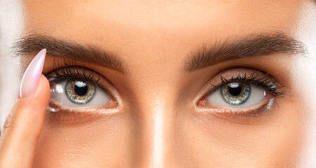 Naklejka premium Beautiful blue eyed young woman holding a contact lens on her finger. Eye care and choice of means to improve vision.