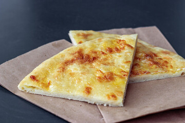 Two pieces of khachapuri on paper bags lie on a black table. Georgian traditional national cuisine.
