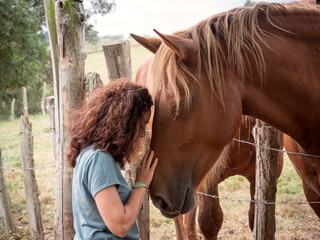 Close up of brunette woman forming bond with a Hispano-Breton horse behind a barb wire fence in a...
