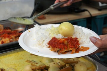 Frauenhände halten weißen Teller mit indonesischem Essen wie weißem Reis, gekochtem Ei,...