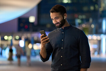 Rich successful indian business man professional entrepreneur wearing earbud standing outdoors on...