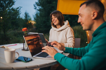 Happy family couple freelancers working laptop on a cozy glamping tent in summer evening. Luxury camping tent for outdoor holiday and vacation. Lifestyle concept