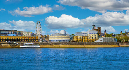 Cologne (Rheinauhafen), Germany - July 9. 2022: Beautiful rhine river waterfront skyline cityscape, ferris wheel, ancient buildings,  flufy cumulus summer clouds