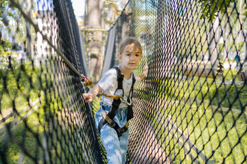 Kid passing the cable route high among trees. Child climbing in high rope course in adventure park....