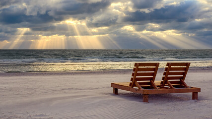 Chaise lounge chair on an empty beach with sun rays in the sky