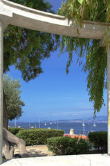Blick durch Säulen in einem Park in Korfu auf Segelyachten in einer Bucht, vertikal 