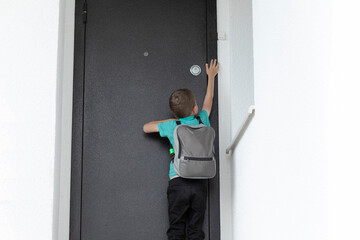 White Caucasian little child, school boy pushes doorbell on closed entrance door, coming back from...