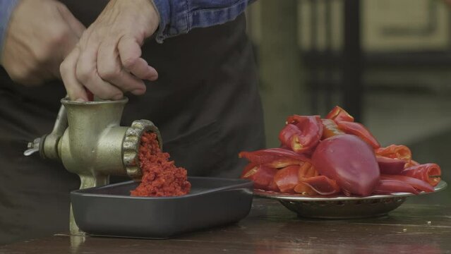 Preparation of homemade sauce with a sweet bell peppers, hot pepper chilli with a grinding machine. Man grinding red peppers on old meat grinder outdoors close-up. Vegetable sauce Healthy organic food