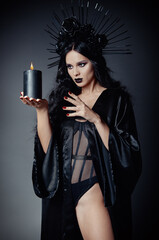 Halloween theme: dangerous young witch dressed in black mantle and headdress with roses and spikes....