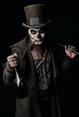 Young man in image of Baron Samedi, the Voodoo deity. Baron Saturday in black coat and top hat with bottle of alcohol and stick in hand. Day of the Dead (and Halloween) theme