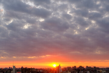 都市の夜明け。日の出とともに空と雲がオレンジ色に染まり、ビル群はシルエットとして写す神戸市街地から芦屋、大阪方面を臨む