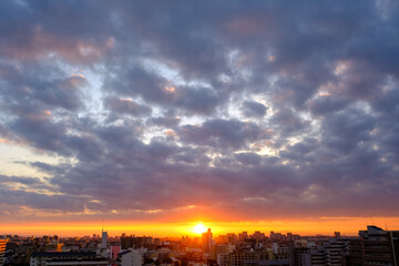 Fototapeta na wymiar 都市の夜明け。日の出とともに空と雲がオレンジ色に染まり、ビル群はシルエットとして写す。神戸市街地から芦屋、大阪方面を臨む