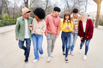 Group of young multiracial friends using mobile phones and walking in a park. Cheerful People having fun outdoors. Concepts of technology addiction in today's lifestyle.