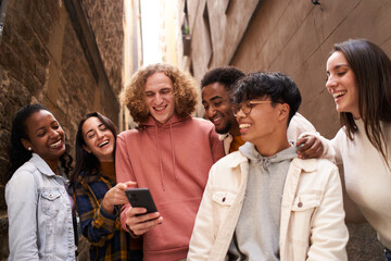 Group of happy young teen people using smartphone outdoors while watching something in mobile and laughing. Concept of technology, friendship and community