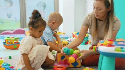 Nursery school. Toddlers and their teacher playing with colorful plastic playhouses, cars and boats. Imagination, creativity, fine motor and gross motor skills development. High quality 4k footage