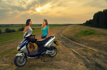 Two young smiling women riding scooter in the summer nature