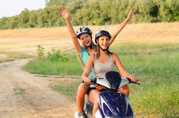 Two young smiling women riding scooter in the summer nature
