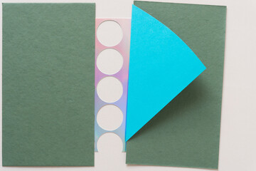 abstract background composed of green card stock, iridescent paper with holes, and a blue paper triangle, flap, or wing on blank paper