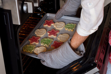 Woman is taking out freshly baked Christmas cookies out of the oven