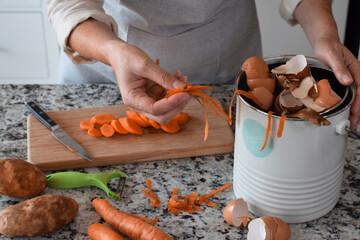 Woman peeling and cutting vegetables in kitchen and using composter for scraps