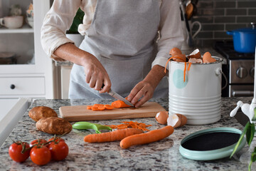 Woman cutting carrots in kitchen and using composter for scraps