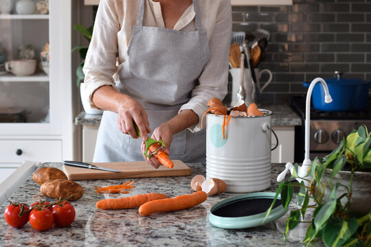 Woman peeling carrots in kitchen and using composter for scraps