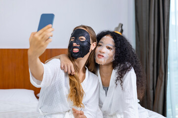 Couple of girlfriend in bathrobe taking selfie doing skincare routine using facial mask on spa holiday for beauty skin and treatment concept