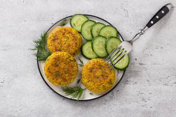 Delicious millet cutlets with carrots and seeds served with cucumber and herbs on a gray textured background, top view. Homemade vegan food - 529727981