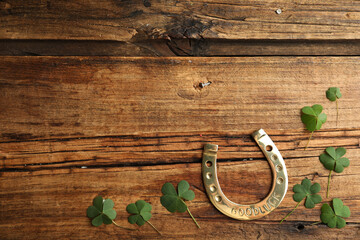 Clover leaves and horseshoe on wooden table, flat lay with space for text. St. Patrick's Day celebration