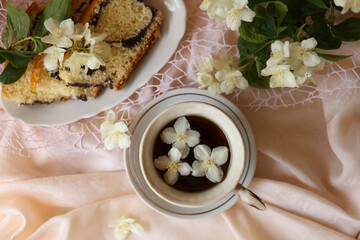 Obraz na płótnie Canvas Cup of aromatic tea, tasty dessert and beautiful jasmine flowers on pink fabric, flat lay