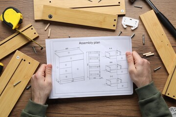 Man with furniture and assembly plan at wooden table, top view