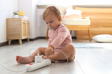 Cute baby playing with charger on floor at home. Dangerous situation