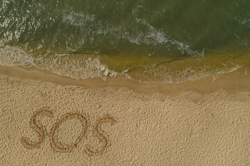 Fototapeta na wymiar SOS message drawn on sandy beach near sea, above view