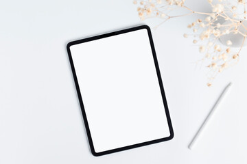 white tablet and stylus with copy space blank screen, light background with dry flower blossoms in vase, top view