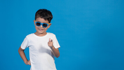 Naklejka premium Hermoso niño con playera blanca y fondo azul. Usando lentes y señalando con su dedo.