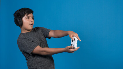 Retrato de estudio de un niño jugando a videojuegos con auriculares y joystick. fondo Azul.