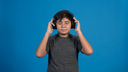 Retrato de estudio de un niño escuchando música tocando con sus manos los audífonos. Con fondo Azul