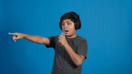 Retrato de estudio de un niño cantando con micrófono y audífonos mientras señala con dedo sobre...