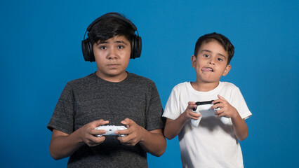 Retrato de estudio de dos niños jugando a videojuegos con auriculares y joystick. Posando en fondo...