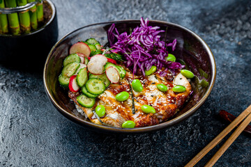 eel poke with rice, edamame,sauce,cabbage and sliced cucumbers on dark stone table