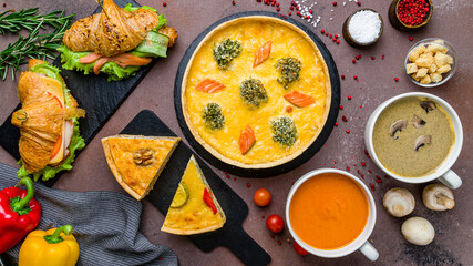 quiche with salmon and spinach, cream soup of mushrooms, tomato cream soup, croissants on brown table top view