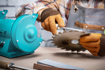  worker sharpens a saw blade with file. man work in workshop. - obrazy, fototapety, plakaty