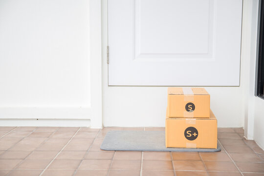 Cardboard Parcel Box Near Door On Floor. Online Shopping, Boxes Delivered To Your Front Door. Easy To Steal When Nobody Is Home. Parcel In Cardboard Box On Doorstep. Delivery Service