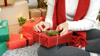 Close up woman hands wrap present gift in cozy living room. Woman wrapping christmas gift box under...