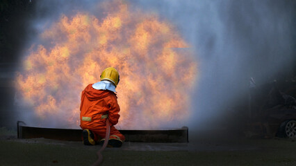 Firefighter Rescue training in fire fighting extinguisher. Firefighter fighting with flame using fire hose chemical water foam spray engine. Fireman wear hard hat, safety suit uniform for protection