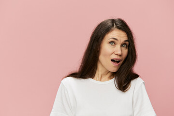 Fototapeta premium horizontal portrait of a cute, attractive, emotional woman on a pink background in a clean white t-shirt, with her mouth wide open