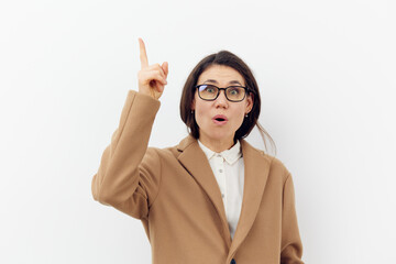a beautiful, pleasant, cute adult woman in an autumn coat and glasses, stands on a light background with an empty space for an advertising layout, raising her index finger up with an enthusiastic face