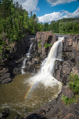 A small rainbow appears in front of High Falls in Pigeon River Provincial Park as the falls plunge down to a pool of water below.
